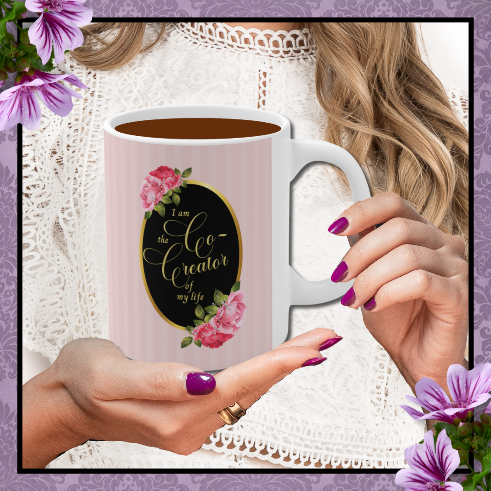 Hands with rose nail polish holding a ceramic mug with saying" I am the co-creator of my life" written in gold lettering on a black oval with gold edge accented with large pink roses at the top and bottom of the oval on a background of pink stripes.