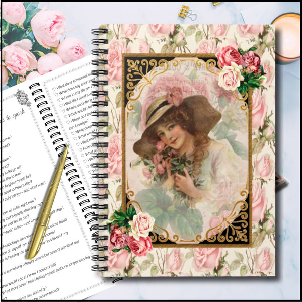 A vintage-style spiral notebook with a floral rose cover and a central portrait illustration, styled on top of an open book with a gold pen.