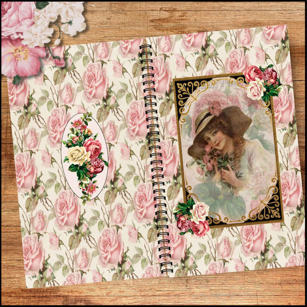 A vintage-style spiral notebook with a pink rose patterned cover, featuring an oval floral emblem on the left and a decorative portrait frame on the right, displayed on a wooden surface.