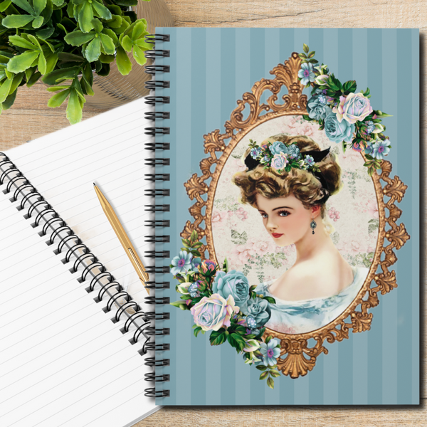 Woman with polished nails holding a Spiral Bound Notebook/Journal featuring a Lovely Victorian image of a Harrison Fisher Illustration surrounded with a gold frame accented with a cluster of blue flowers on a blue striped background laying on top of open spiral notebook