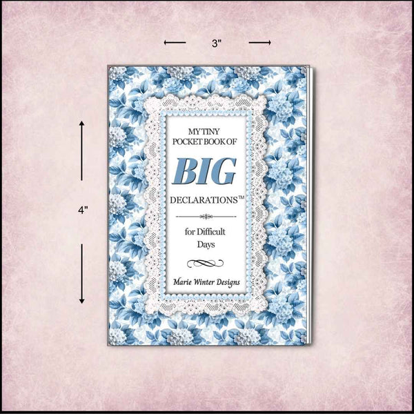 A pocket book with a blue floral border and lace-style center panel, shown on a pale pink textured background with dimension arrows indicating 3 by 4 inches. The cover reads 'My Tiny Pocket Book of Big Declarations for Difficult Days' by Marie Winter Designs.