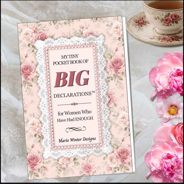 A decorative pocket book titled "My Tiny Pocket Book of Big Declarations for Women Who Have Had Enough" by Marie Winter Designs, shown standing upright on a lace-covered surface with pink roses around it and a teacup in the background.