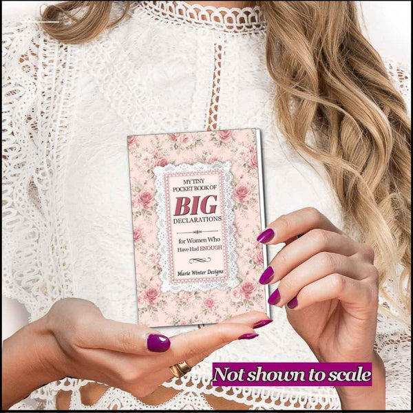 A woman in a white lace top holds a slim pocket book titled 'My Tiny Pocket Book of Big Declarations' with a pink floral cover. The photo is cropped to show her hands, hair, and clothing, with a purple 'Not shown to scale' banner at the bottom.