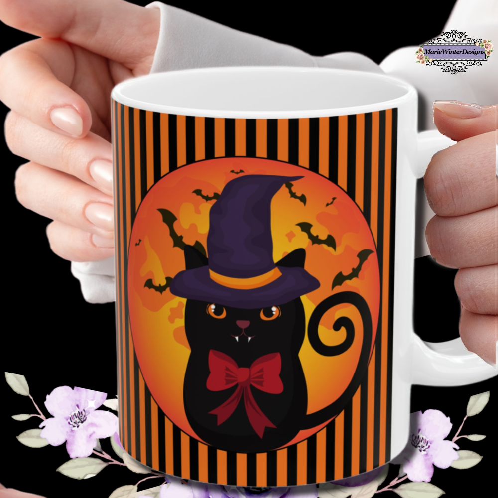 Hands holding a Halloween mug with black cat wearing a purple pointed had and a red bow around neck in side a circle with bats flying behind on an orange and black stripe background with a white handle