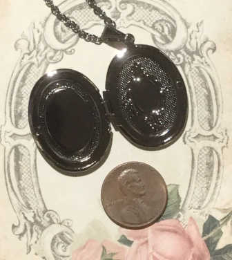 Open vintage oval locket necklace with antique silver-tone finish shown beside a penny for size reference.