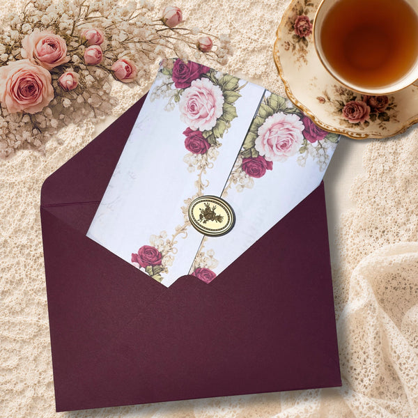 Open burgundy envelope holding a floral letter sealed with a gold emblem, arranged on an ivory lace doily background.