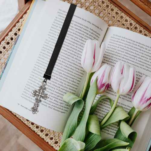 A black ribbon bookmark with a silver cross pendant rests on open book pages, styled with white tulips with pink stripes on a wooden tray with a woven mat.