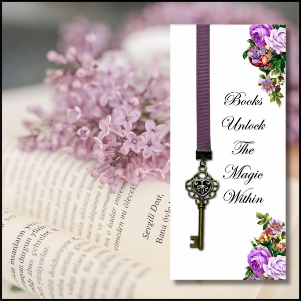 A decorative book bookmark with a purple ribbon and antique-style metal key, shown over a blurred open book with pink flowers. The bookmark has a white panel with the phrase 'Books Unlock The Magic Within' and purple floral corner accents.