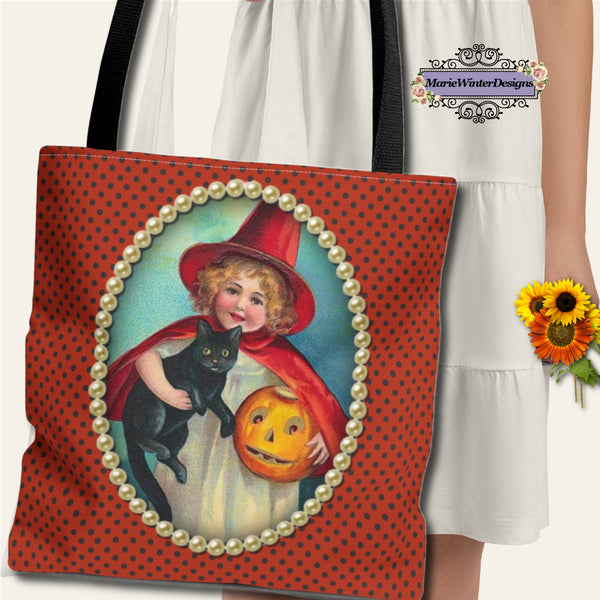 A person in a white dress holds a Halloween-themed tote bag with a vintage witch design, featuring a girl with a black cat and a jack-o-lantern, framed by pearls on a polka-dot orange background.