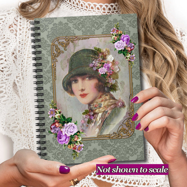 A person holds a spiral-bound notebook featuring a vintage-style portrait of a woman in a hat with purple flowers, set against a lace-trimmed background. A purple text banner at the bottom reads 'Not shown to scale'.