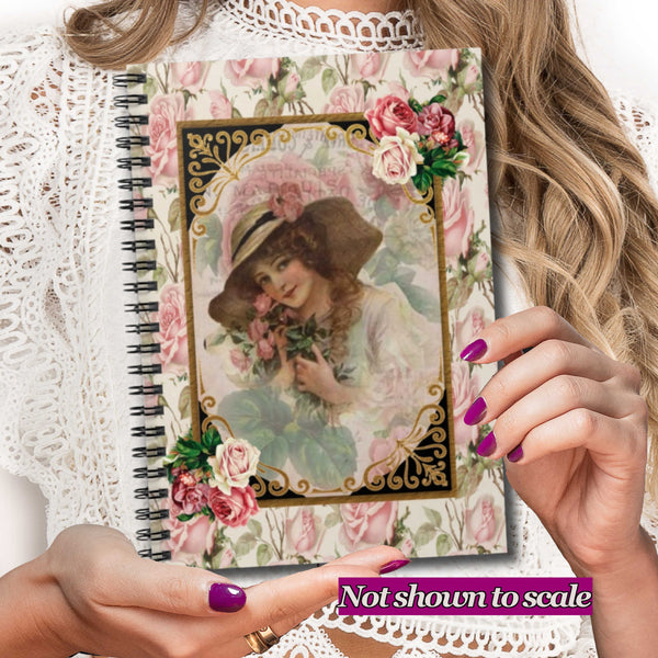 A vintage-style spiral notebook with a floral pink cover and an illustration of a woman in a hat, held by hands with purple nail polish over a white lace top. A purple text overlay at the bottom reads 'Not shown to scale'.