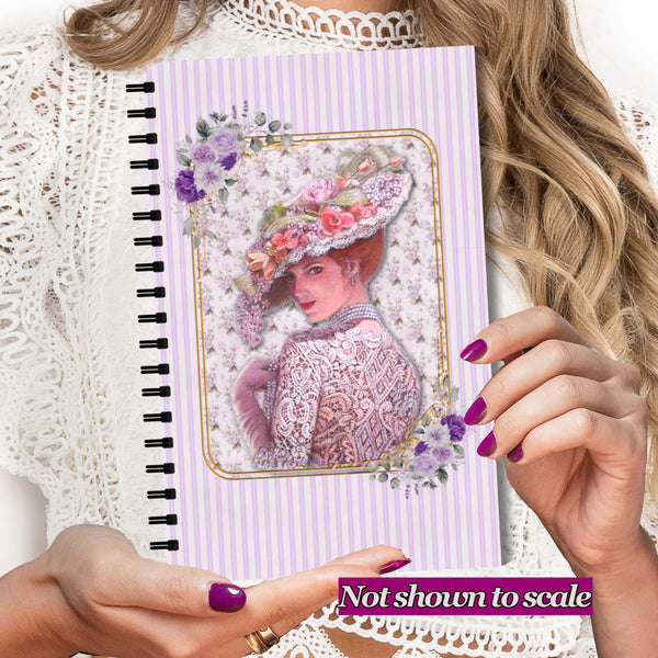 A person holds a spiral-bound notebook with a lavender and white striped cover featuring an illustration of a woman in an ornate floral hat. The person wears a white lace top, and a purple banner at the bottom reads 'Not shown to scale'.