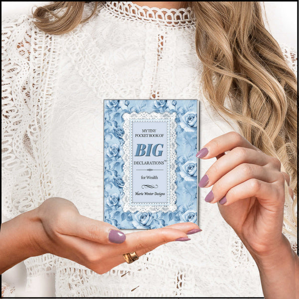 A woman in a white lace top holds a small pocket book titled "My Tiny Pocket Book of Big Declarations" with a pink floral cover, using both hands to present it.