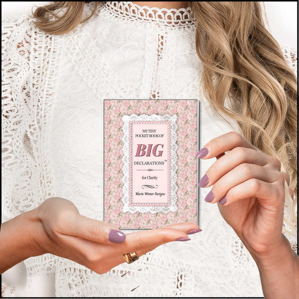 A woman in a white lace top holds a slim book titled "My Tiny List of Big Declarations" with a pink floral cover. The photo is styled as a close-up lifestyle shot with the woman's hands and hair visible.