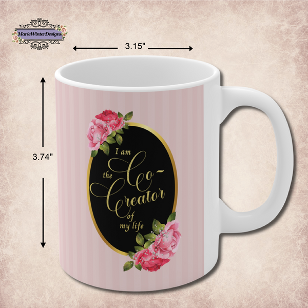 Measurements of a ceramic mug with saying" I am the co-creator of my life" written in gold lettering on a black oval with gold edge accented with large pink roses at the top and bottom of the oval on a background of pink stripes.