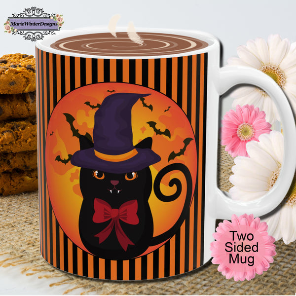 Halloween mug with black cat wearing a purple pointed had and a red bow around neck in side a circle with bats flying behind on an orange and black stripe background with a white handle in front of a pile of chocolate chip cookies and pink and white flowers.