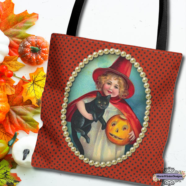 Halloween tote bag with a vintage witch design, showing a girl holding a black cat and jack-o-lantern, framed by pearls. Autumn leaves and pumpkins are beside the bag