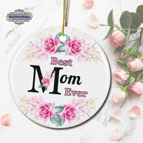 A "Best Mom Ever"; floral ornament featuring pink roses and greenery is displayed on a marble background with scattered pink petals and a bouquet of roses. The ornament hangs by a gold string, and the MarieWinterDesigns logo appears in the corner.