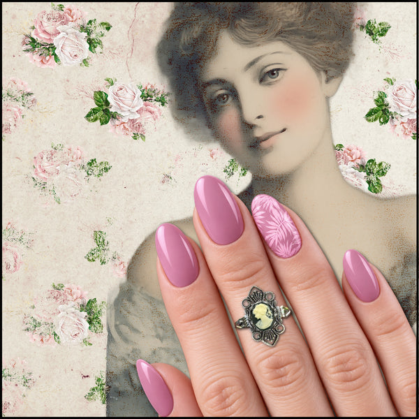 A close-up of a hand with manicured nails in dusty pink and floral pink designs, wearing a silver ring with a cameo-style face, set against a vintage-style illustration of a woman and a pink rose pattern.