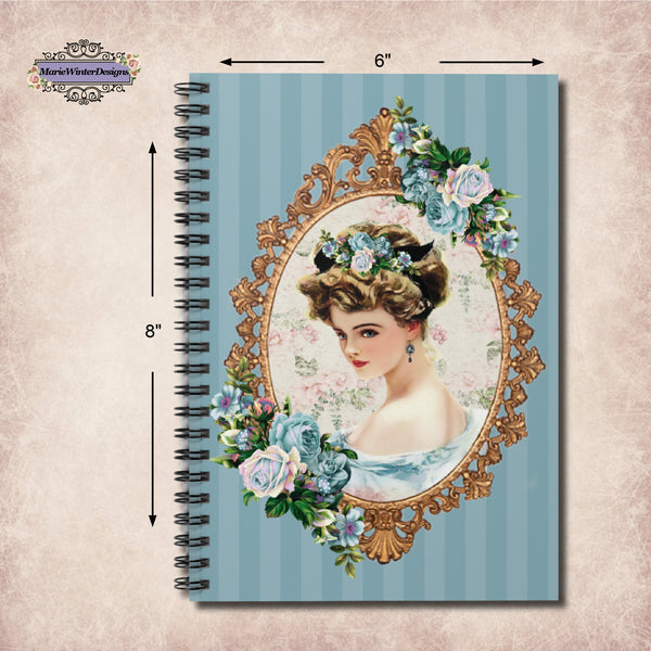 Measurements of Woman with polished nails holding a Spiral Bound Notebook/Journal featuring a Lovely Victorian image of a Harrison Fisher Illustration surrounded with a gold frame accented with a cluster of blue flowers on a blue striped background