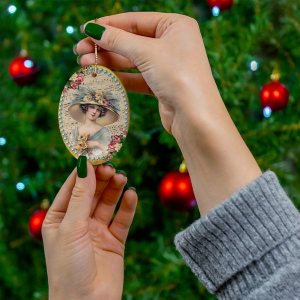 hands holding a Ceramic Ornament With Elegant Early 1900s Vintage Harrison Fisher Illustration of Lady Holding a Rose surrounded by light teal pearls in front of Christmas tree