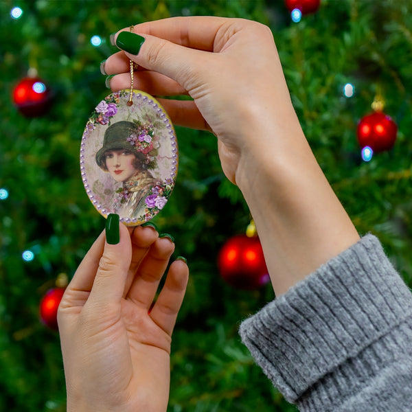 hands holding a Ceramic Ornament With Elegant Early 1900s Vintage Woman in Green Flapper Style Gatsby Hat surrounded by purple pearls on gold background in front of Christmas tree