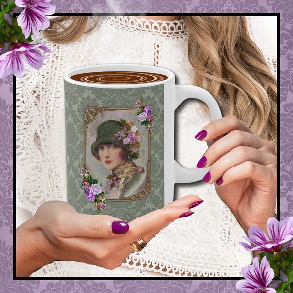 Hands with dark rose nails holding a Ceramic Mug With Elegant 1920s Vintage Woman in Green Flapper Style Gatsby Hat surrounded by a gold art deco style frame accented with vintage purple flowers on green damask background with white handle